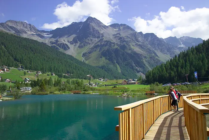 Urlauber auf einer Holzbrücke über einem See mit Bergblick im Sommer